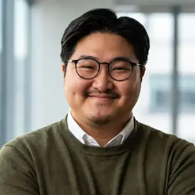 Professional headshot of a team member wearing round glasses and an olive-green sweater